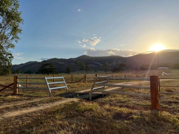 Sunset over a rural field with metal gates and hills in the background.