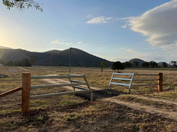 Open metal farm gate with hills and clear sky in the background.