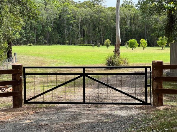 Black metal gate blocking driveway to a green grassy field with trees.