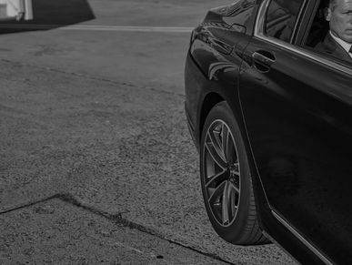 Close-up of a black car's rear wheel and side with a partial view of a person inside.