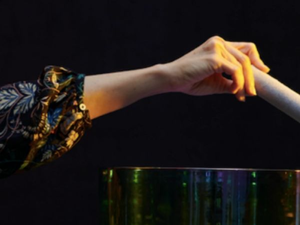 Hand holding a stick above a glass bowl against a dark background.