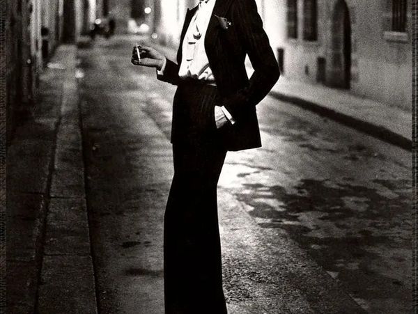 A person in a suit smoking on a dimly lit street at night.