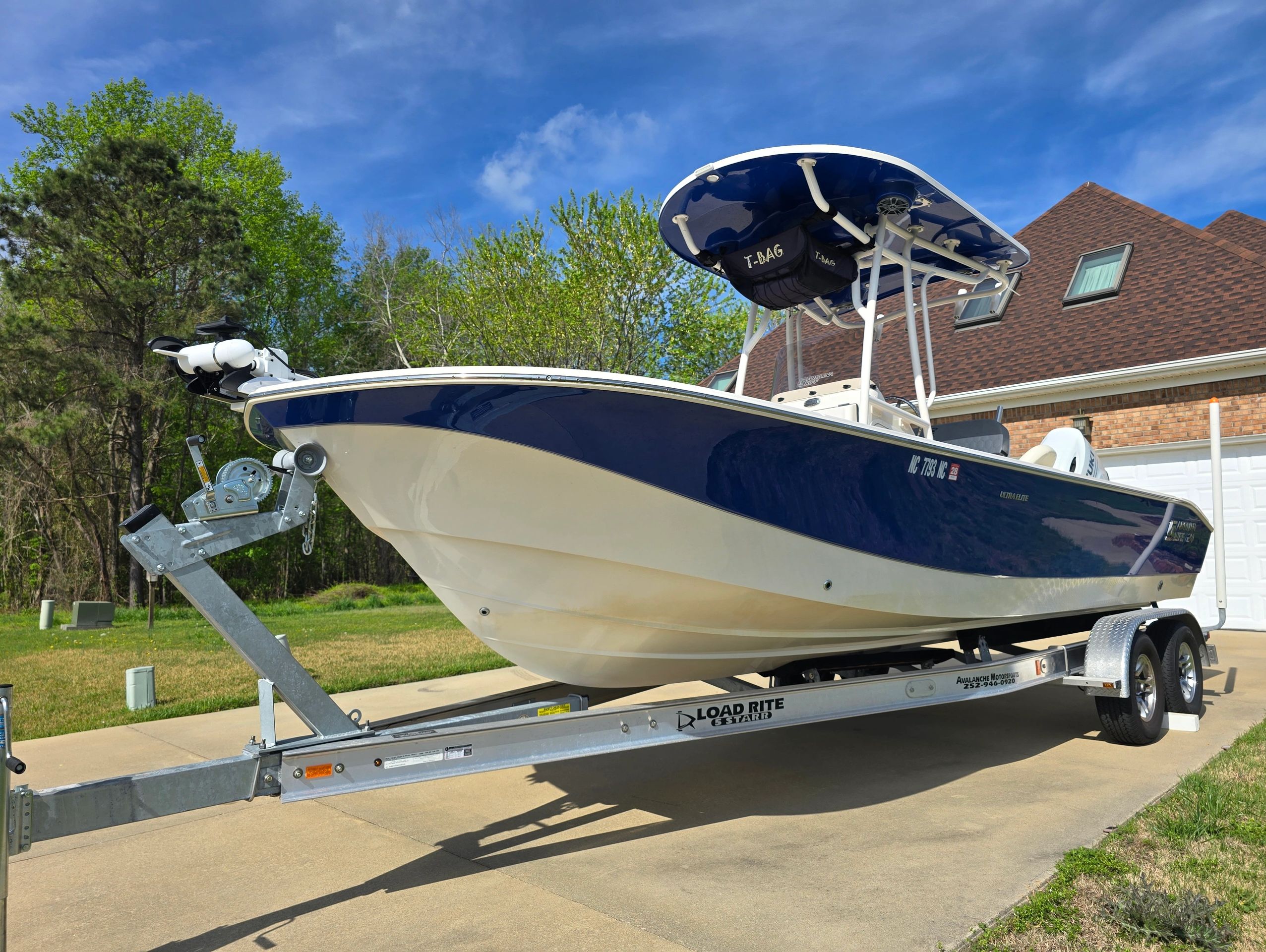 A blue and white fishing boat on a trailer in a driveway on a sunny day.