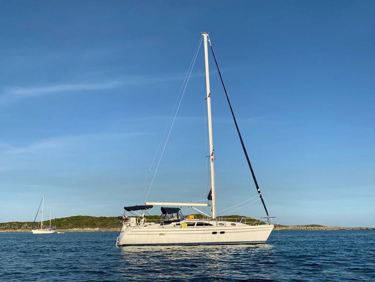 A sailboat on calm water near a small island under a clear blue sky.