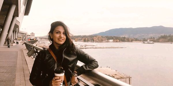 Woman in black jacket enjoying a waterfront view with mountains in the background.