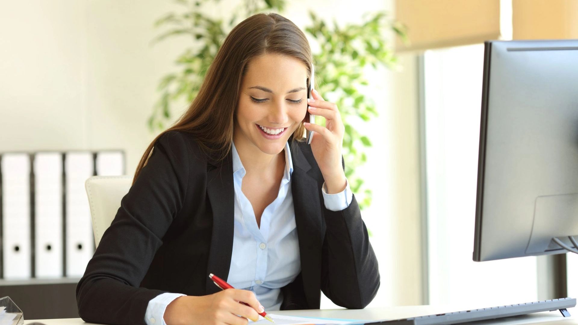 Woman smiling while talking on phone and writing.
