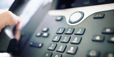Close-up of a hand dialing a number on a phone keypad.