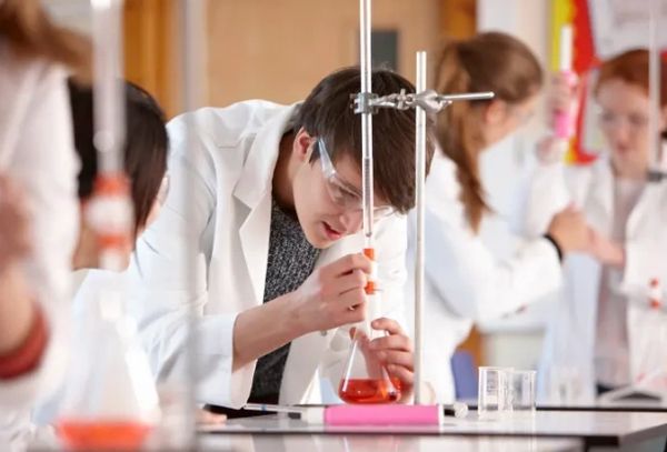 Student conducting chemistry experiment with orange liquid in lab.