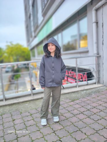 A young girl in a hoodie and cargo pants stands outdoors on a paved surface.