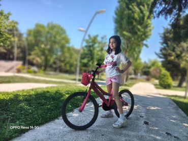 Young girl posing with her pink bicycle in a sunny park.