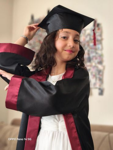 Young girl in graduation gown and cap smiling confidently.