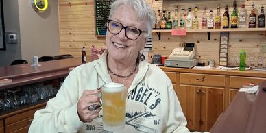 Elderly man smiling with a beer mug in a cozy bar.