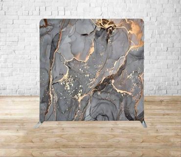 Decorative backdrop with gray and gold marbled pattern against a white brick wall.