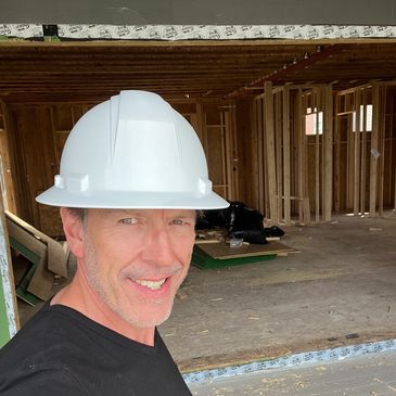 Man wearing a white hard hat inside a wooden frame construction site.
