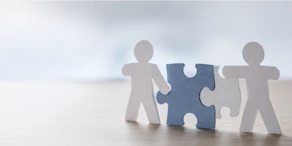 Paper figures holding puzzle pieces symbolizing teamwork.