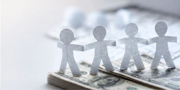 Paper chain figures stand on stacks of US dollar bills symbolizing financial unity.