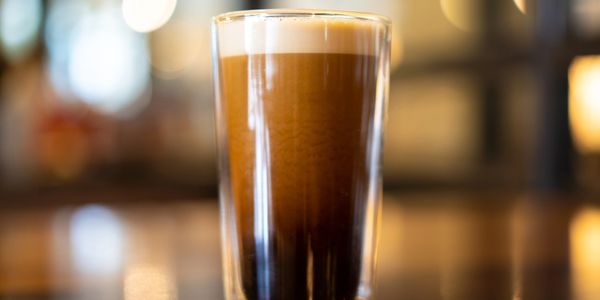 A glass of layered coffee with frothy top on a blurred background.