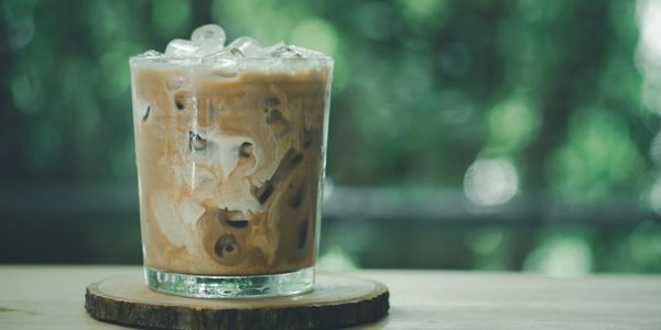A glass of iced coffee with milk on a wooden coaster.
