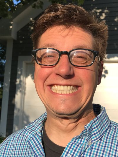Man smiling widely wearing glasses and checkered shirt.