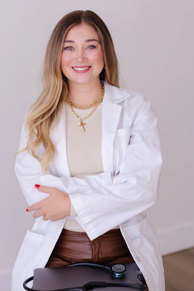 Smiling female nurse practitioner in white coat with stethoscope and laptop.