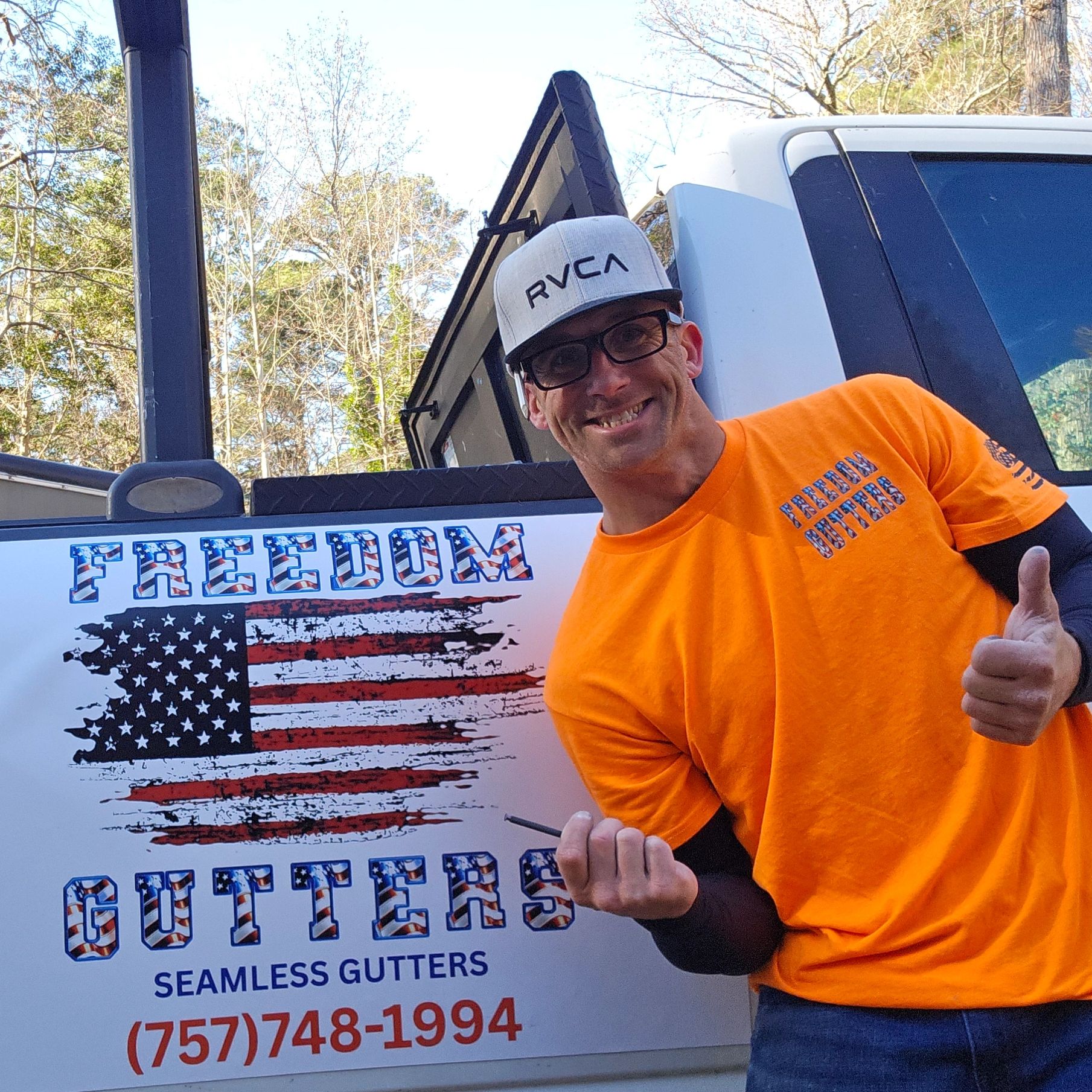 Man in orange shirt giving thumbs up by a patriotic Freedom Gutters sign.