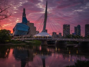 A picturesque sunset view of the Esplanade Riel pedestrian bridge in Winnipeg, Canada. The sky is il