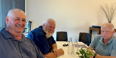 Three elderly men sitting around a table smiling.