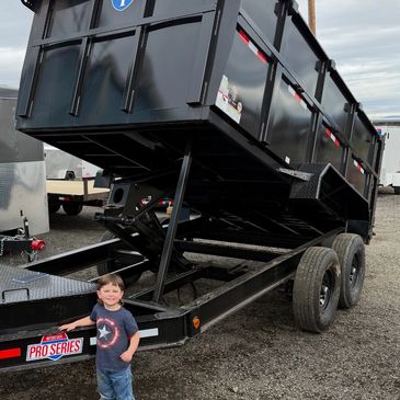 A smiling child stands next to a large black dump trailer with 'Pro Series' label.
