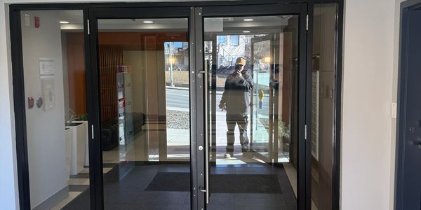 Man reflected on glass doors entering a building lobby.