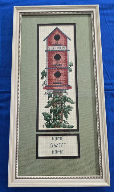 Framed cross-stitch of a birdhouse and 'Home Sweet Home'.