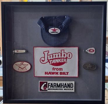 Framed Hawk Bilt merchandise including cap, patches, and pins.