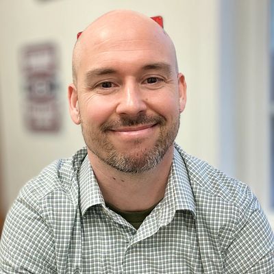 Smiling bald man in a checkered shirt sitting indoors.