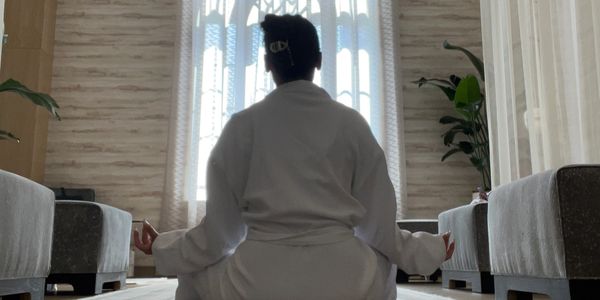 Person meditating in a serene, sunlit room with a large arched window.