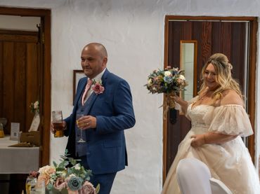 Bride and groom at their wedding reception, holding drinks and bouquet.
