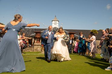 Newlyweds walk under confetti shower after wedding ceremony outdoors.
