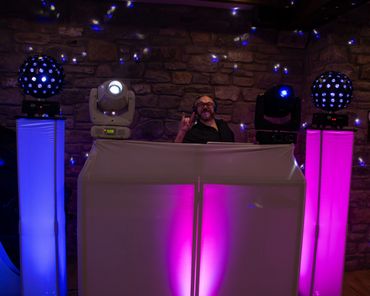 DJ performing with colorful lights and a stone wall background.