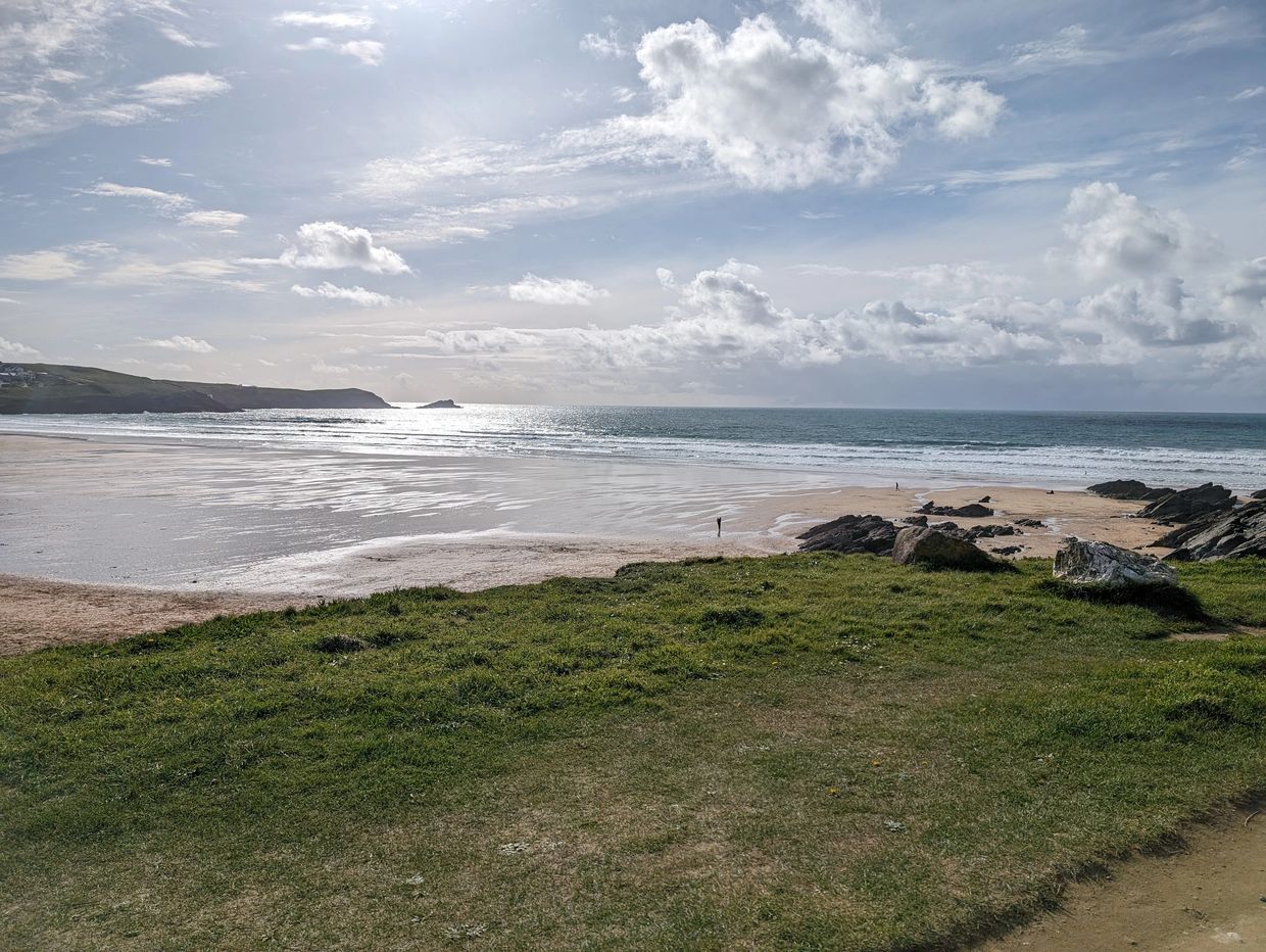 Bright day on a Cornish beach with the sea coming to shore. Grass and nature