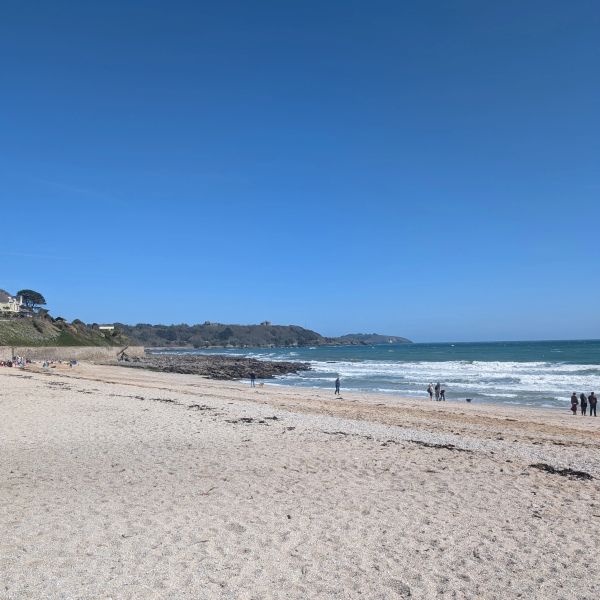 Sunny day at a peaceful, sandy beach with a few people walking by the shore. Cornwall, UK