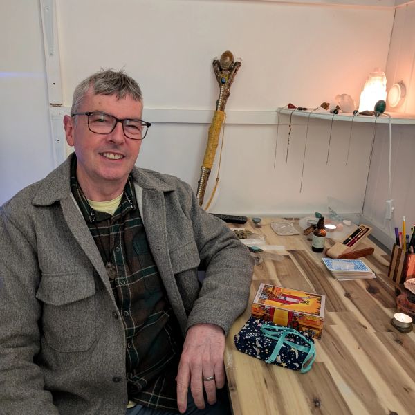 Man smiling at a desk with tarot cards and candles. Spiritual Healer UK