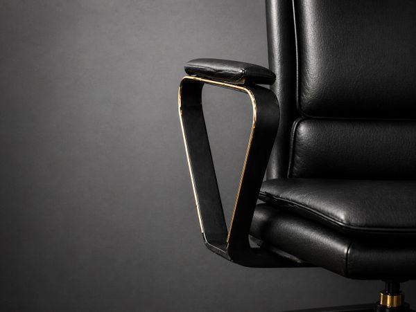 Close-up of a black leather office chair armrest against a dark background.