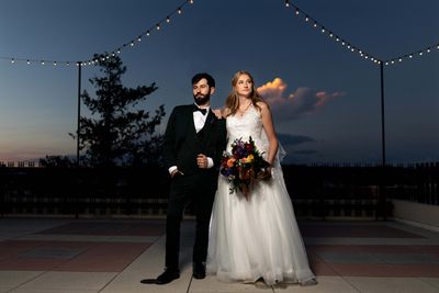 Bride and groom posing under string lights at dusk.