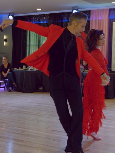 A couple elegantly dancing indoors, dressed in red and black.