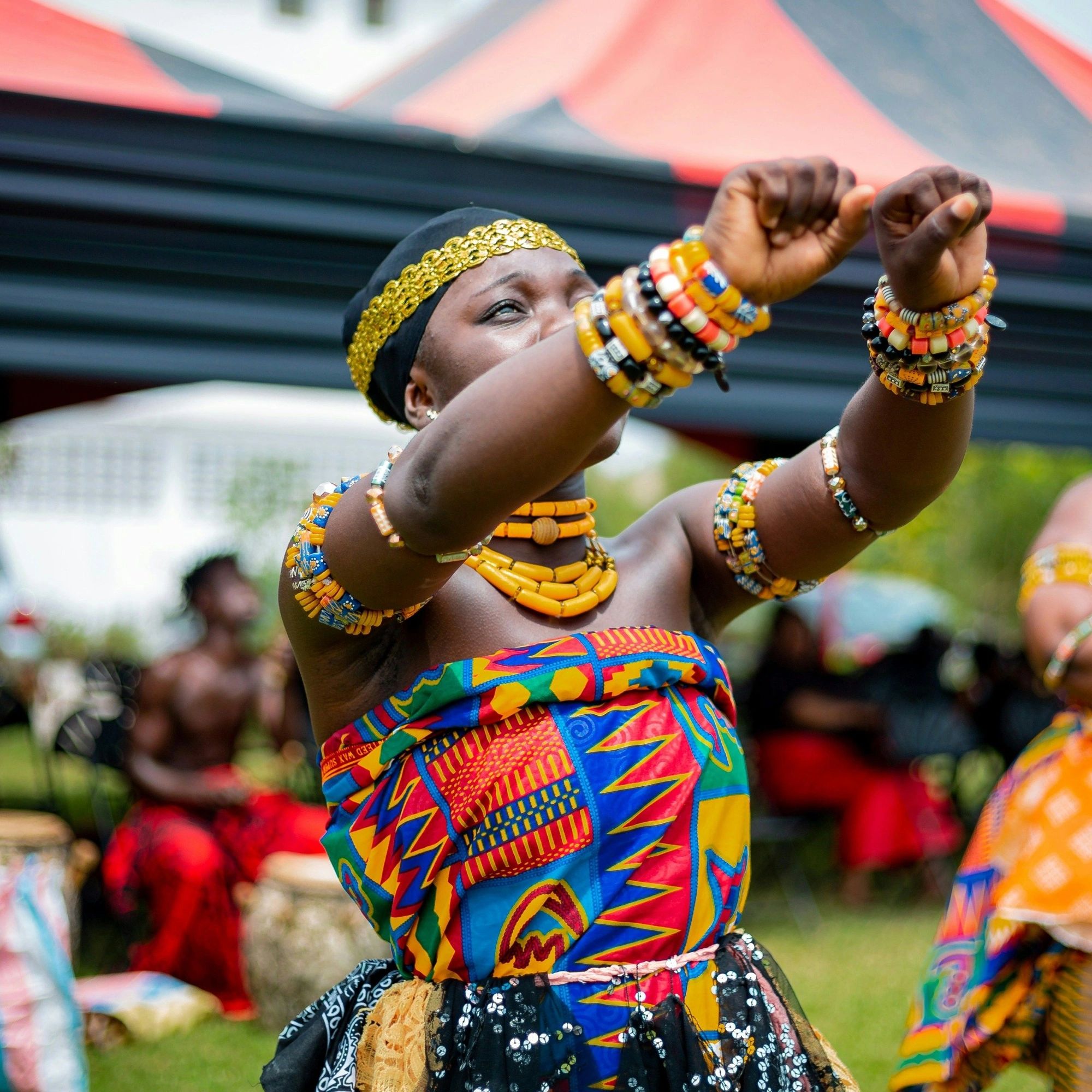 Woman in vibrant traditional attire dancing with colorful beads and bracelets.