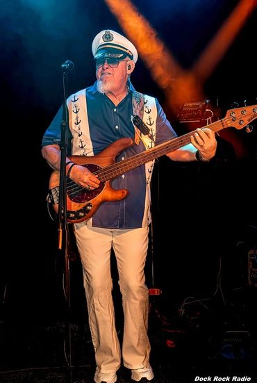 Musician in nautical attire playing bass guitar on stage.