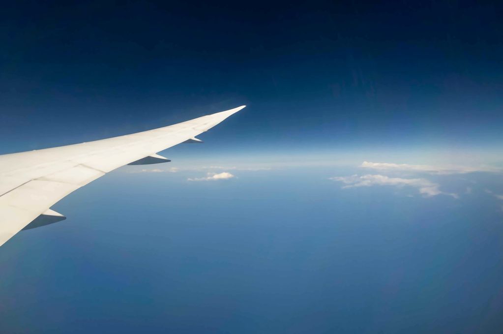 View from an airplane window showing the wing and blue sky above clouds.