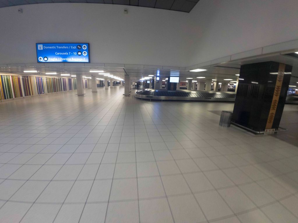Empty airport baggage claim area with signage and colorful wall art.