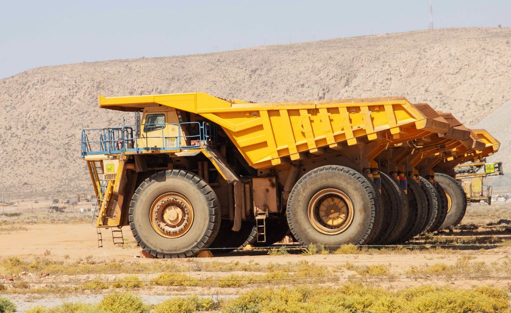 A row of large yellow mining dump trucks parked in a desert area.