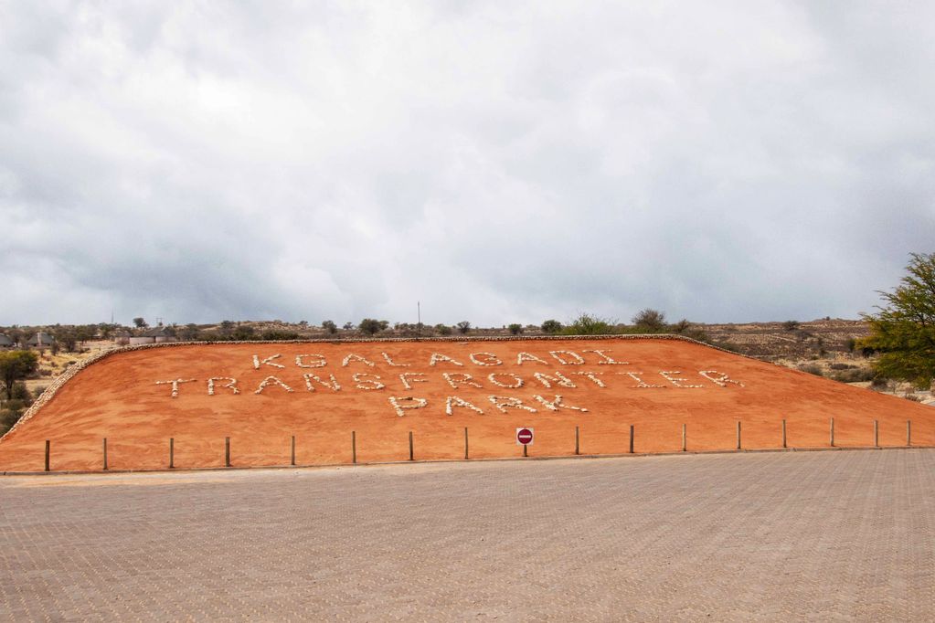 Sign made of stones reading 'Kgalagadi Transfrontier Park' on a red earth hill.