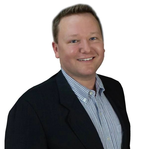 Smiling man in business attire with a striped shirt and black blazer.