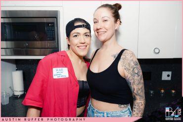 Two smiling women posing together in a kitchen setting.